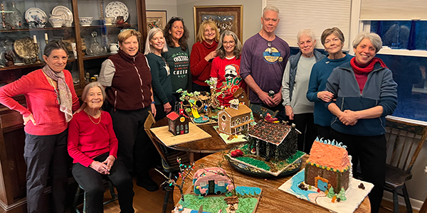 Neighbors gathered around a table of decorated gingerbread houses